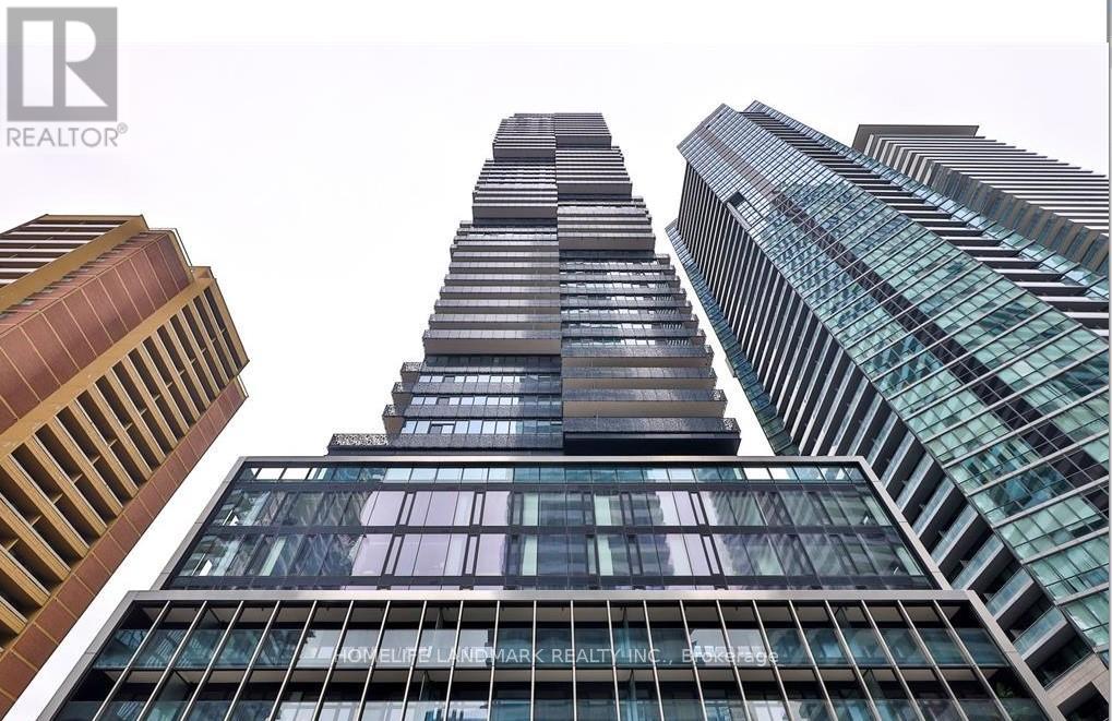 A tall building with a glass facade stands in front of other buildings.