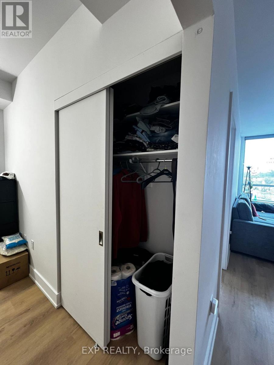 A white closet with a door open showing clothes and a trash can.