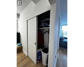 A white closet with a door open showing clothes and a trash can.