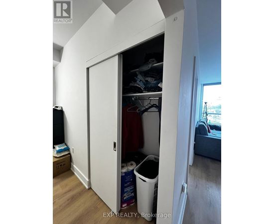 A white closet with a door open showing clothes and a trash can.
