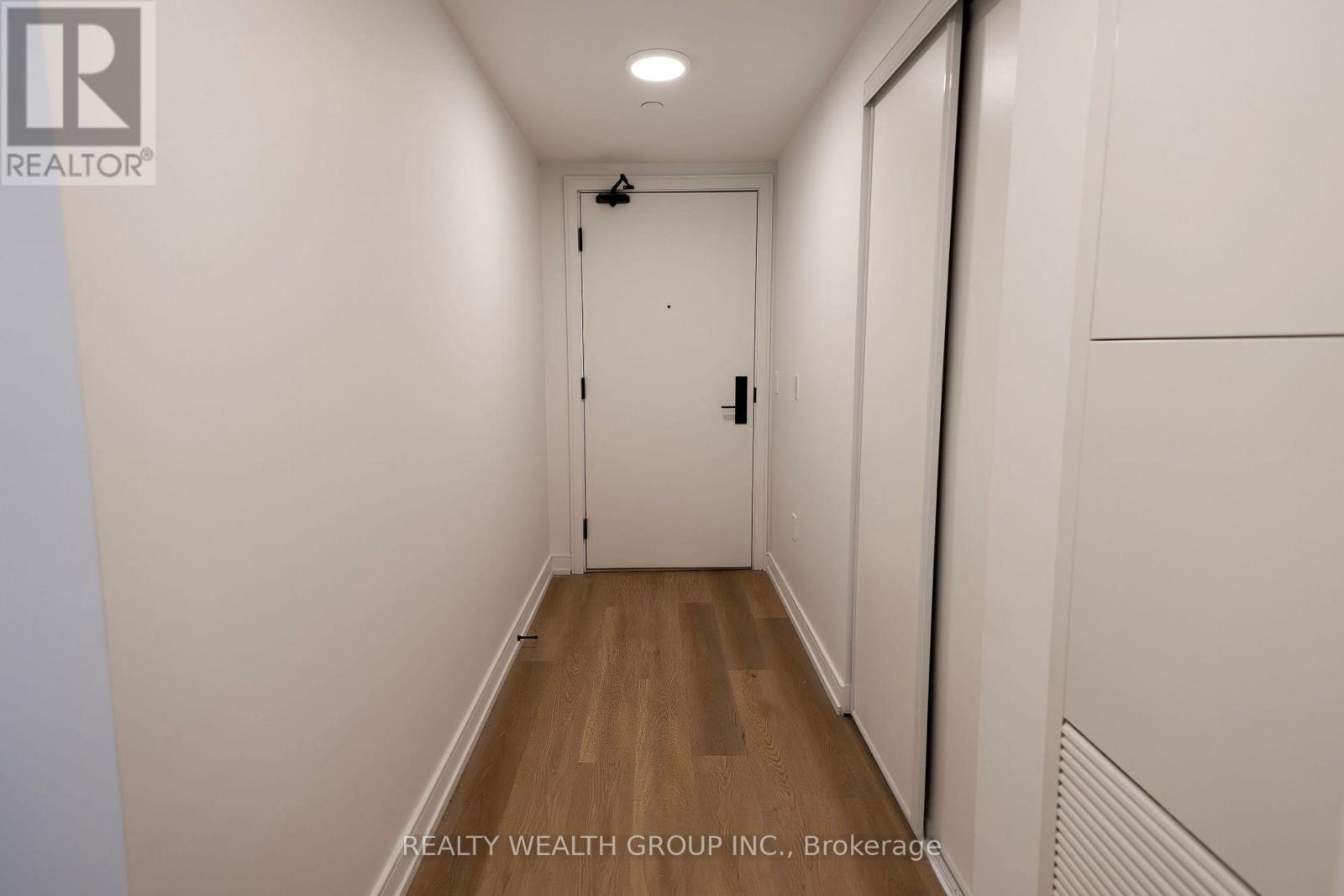 A hallway with a door at the end and a Realty Wealth Group Inc. logo on the wall.