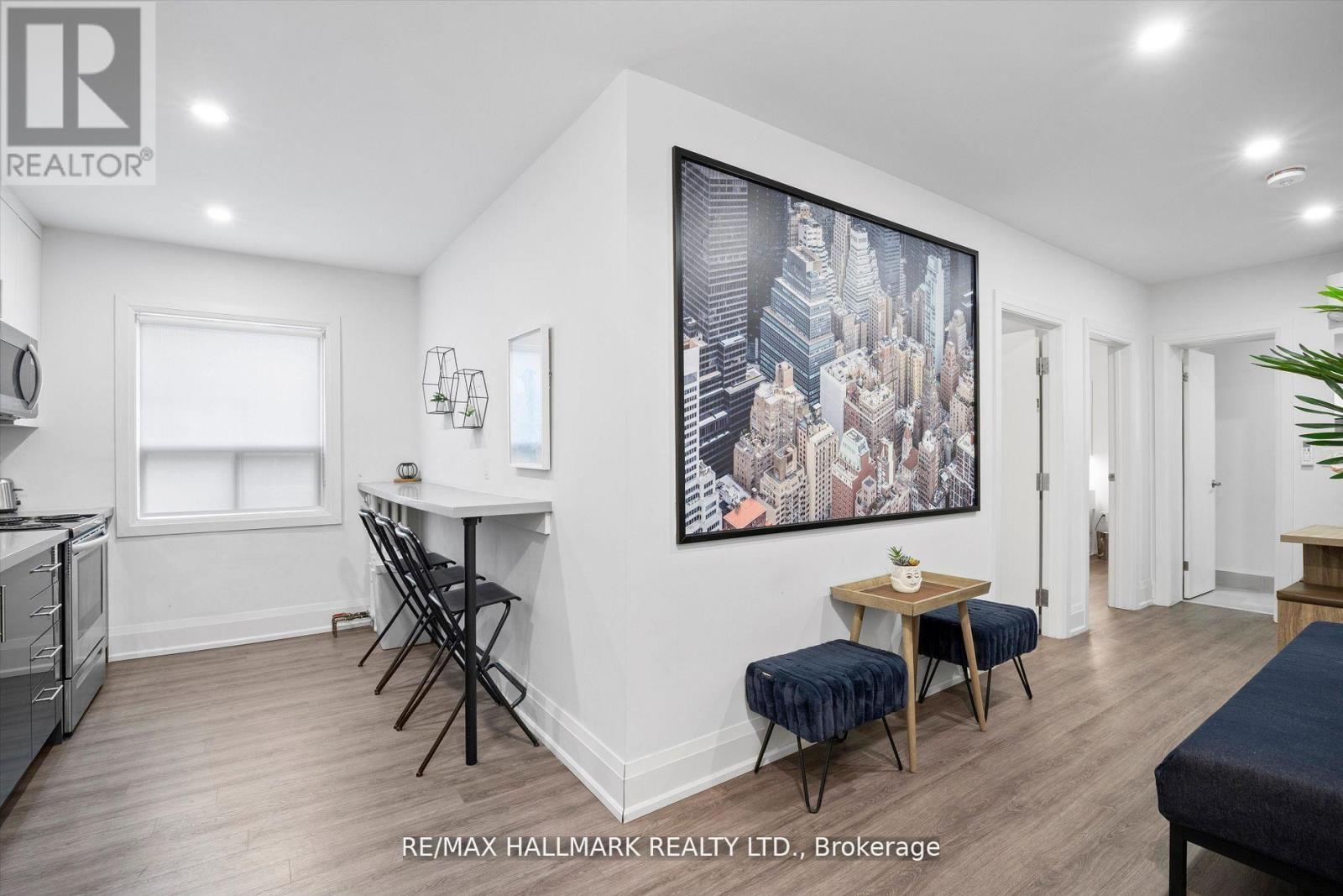 A well-lit, spacious room with a dining table and chairs, a kitchen area, and a large cityscape painting on the wall.