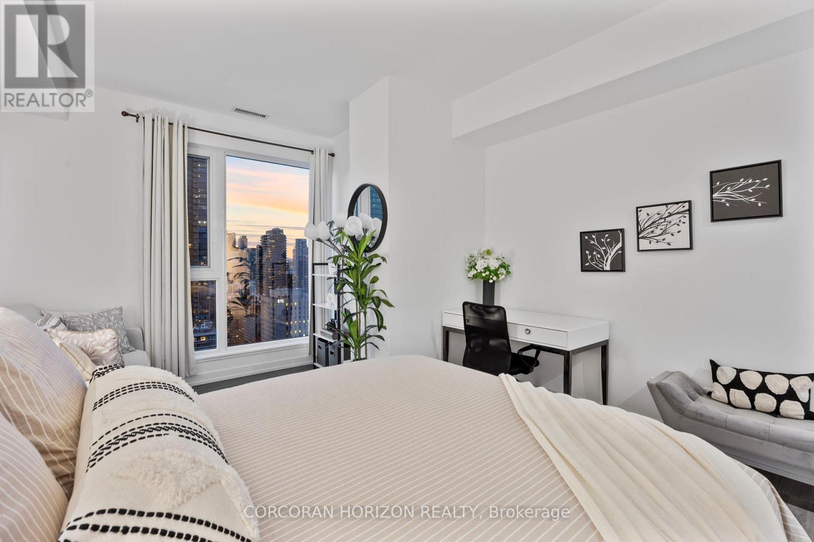A bedroom with a large bed and a city view through the window.