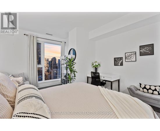 A bedroom with a large bed and a city view through the window.