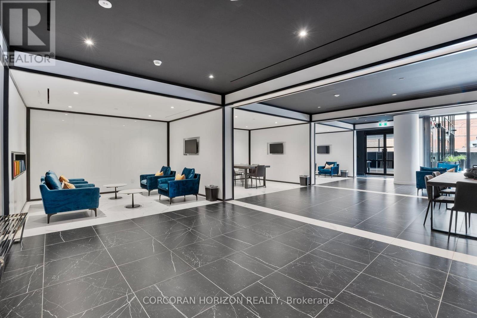 A spacious lobby with blue chairs and a black and white floor.