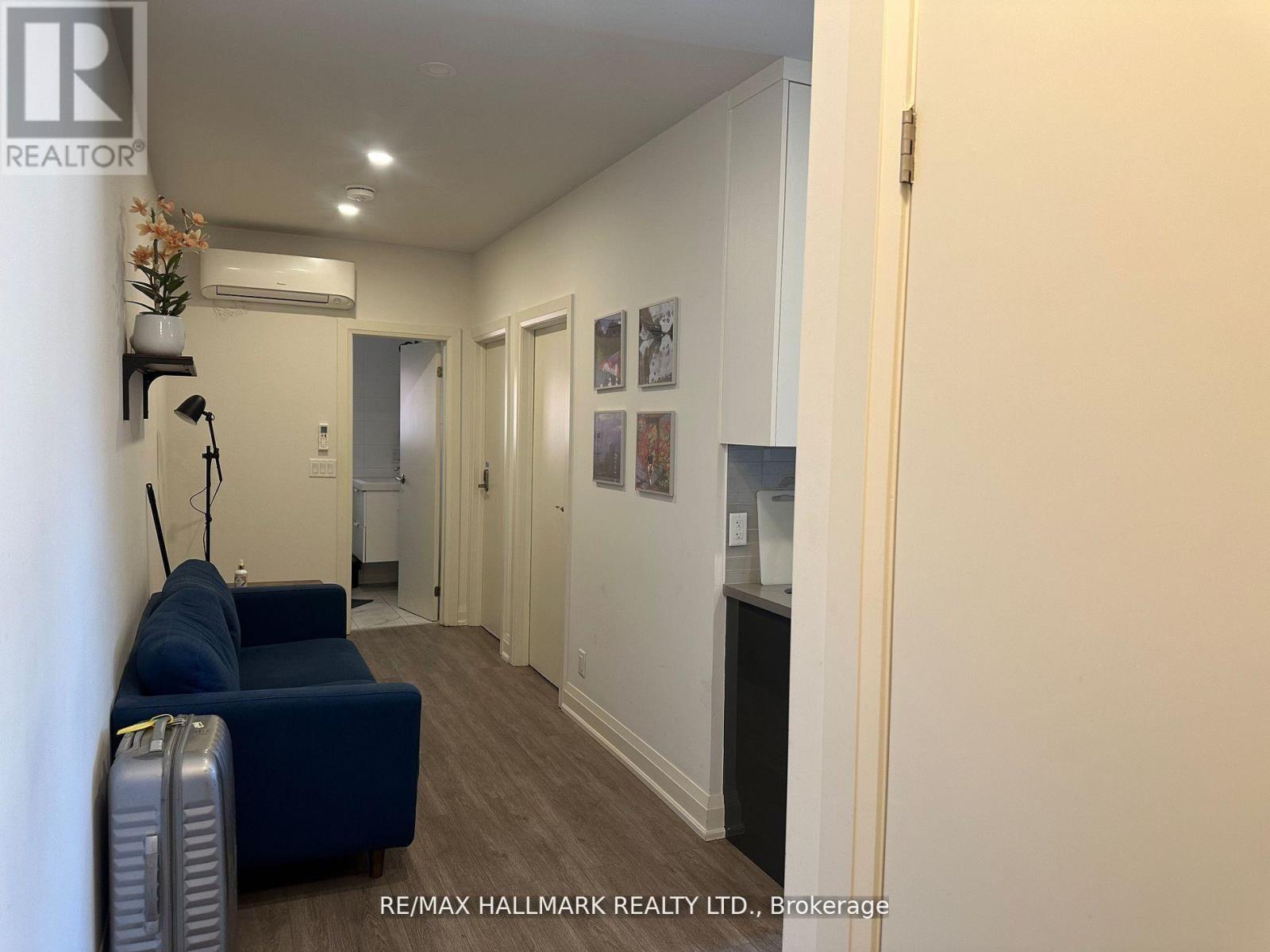 A blue sofa sits in a well-lit hallway with a RE/MAX Hallmark Realty Ltd. sign on the wall.