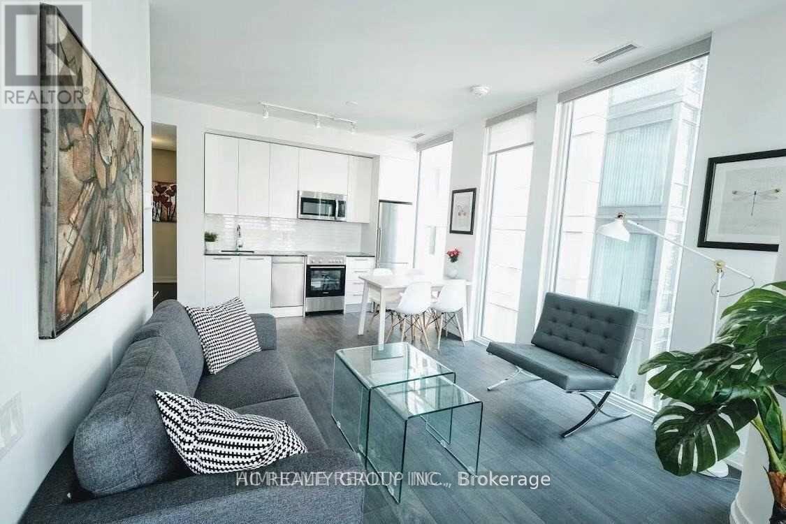 A modern living room with a grey couch, a glass coffee table, and a large painting on the wall.
