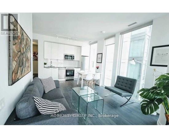 A modern living room with a grey couch, a glass coffee table, and a large painting on the wall.