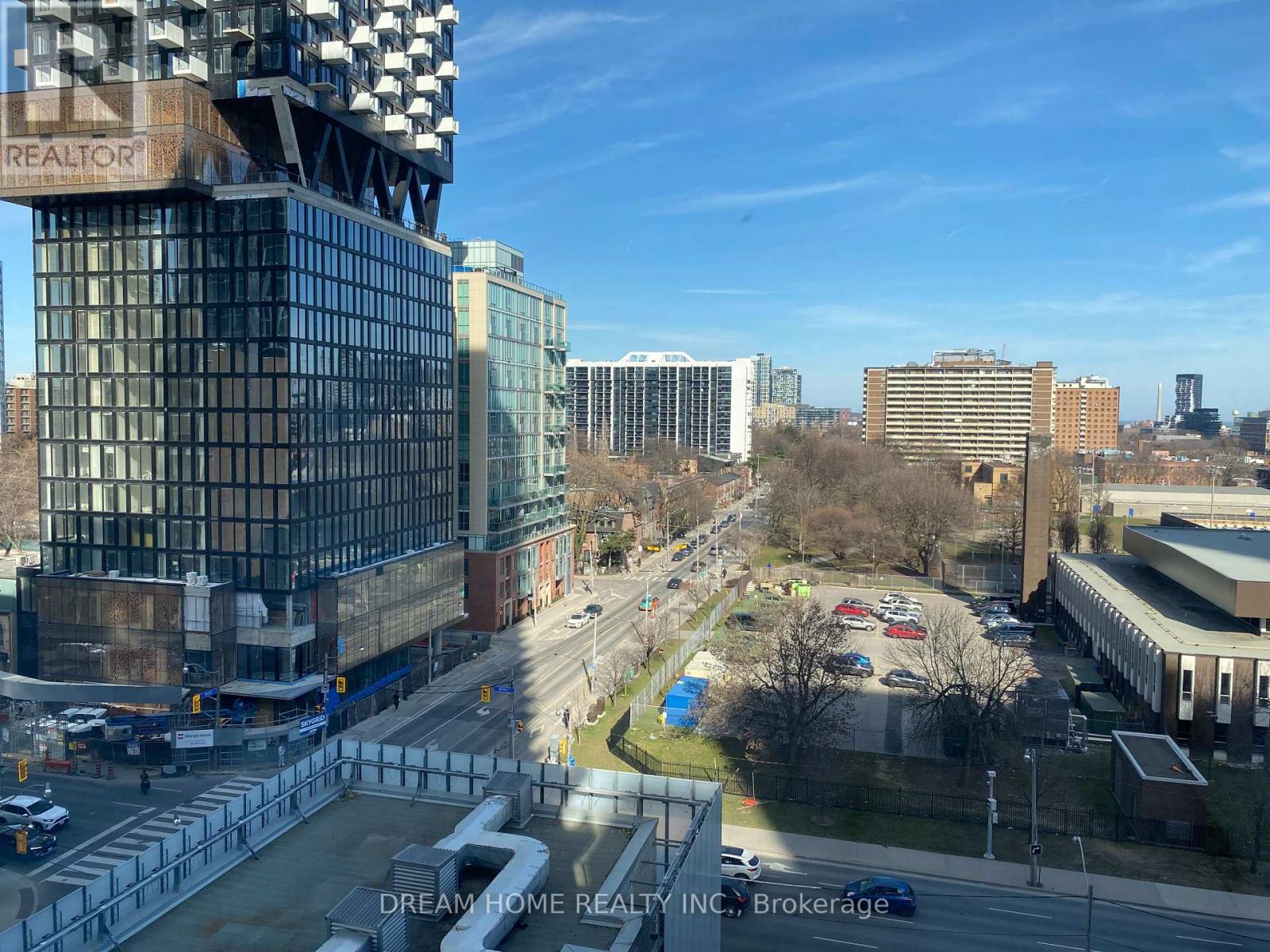 A city street with a large building on the left and a parking lot in the foreground.
