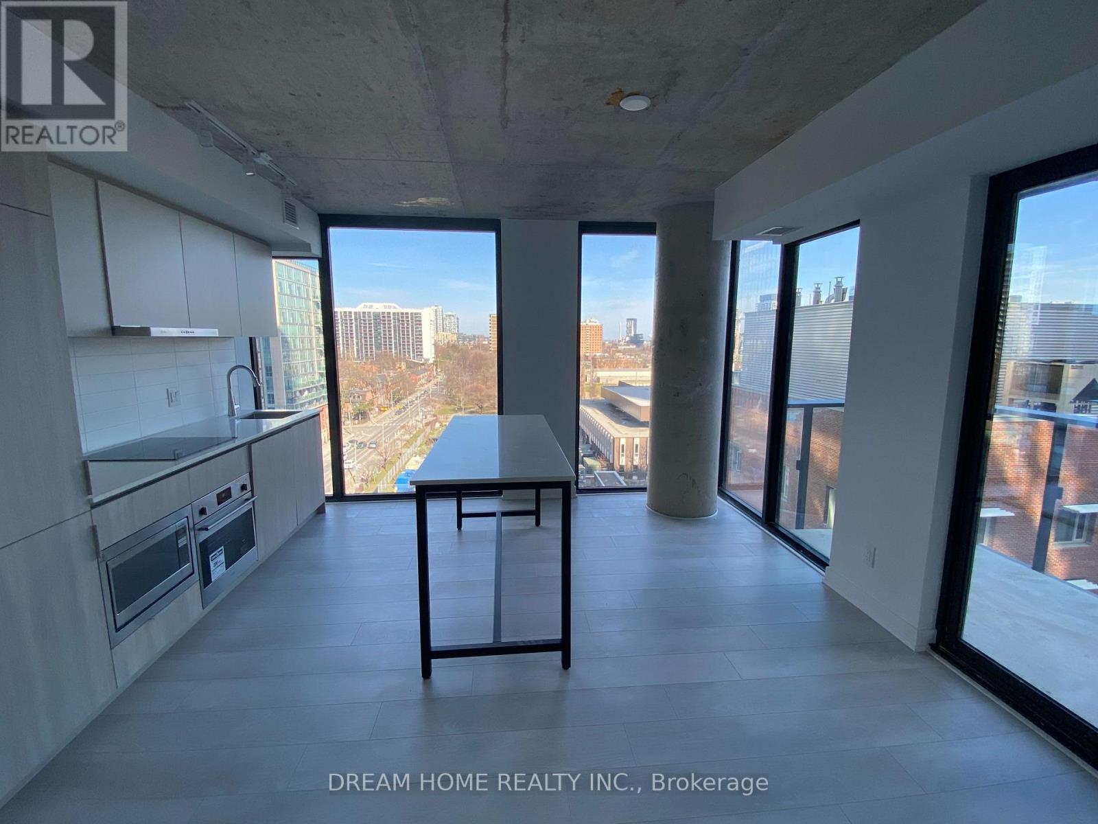A modern kitchen with a table and chairs in the foreground and a view of the city through the windows.