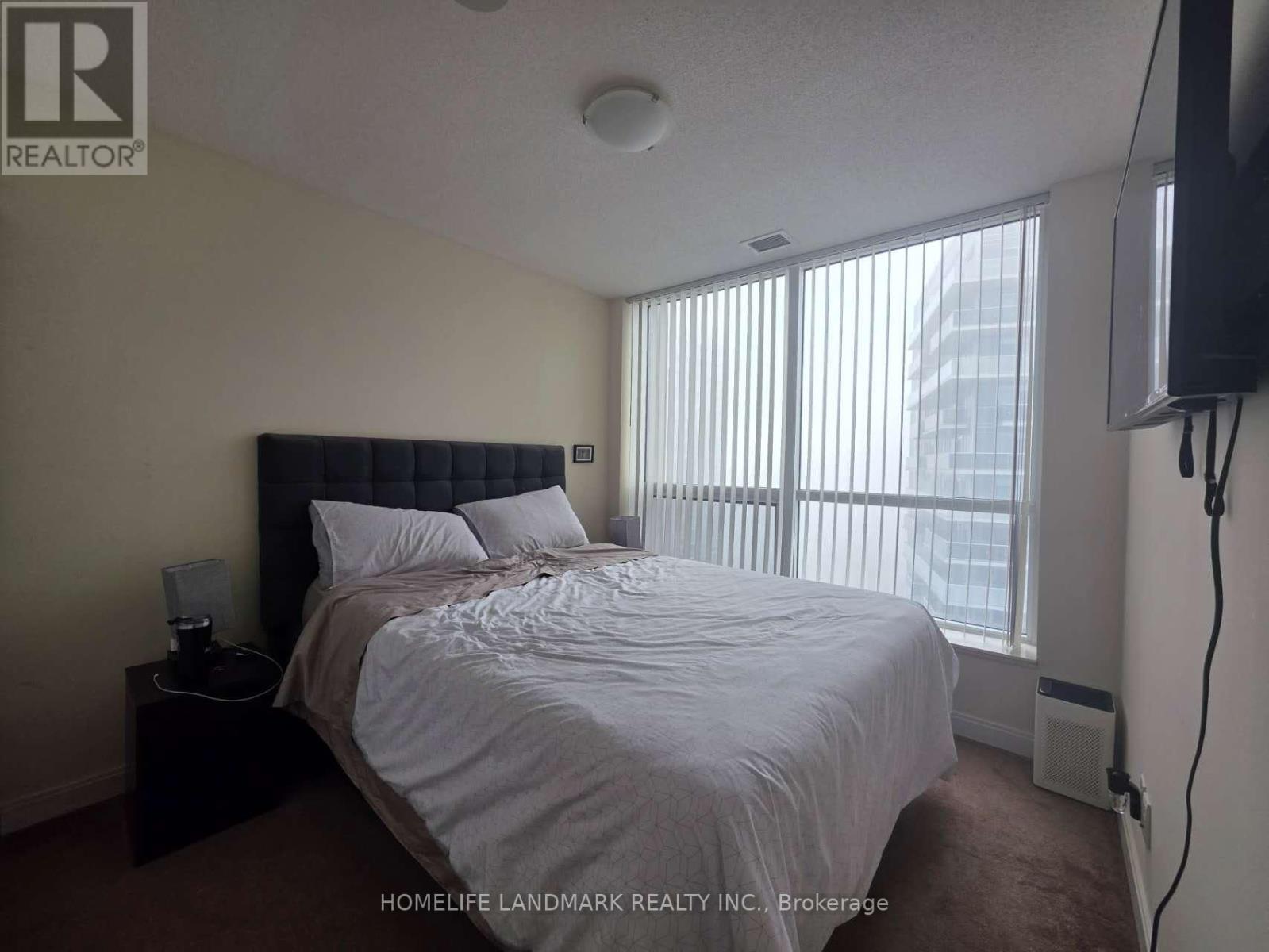 A bedroom with a large bed and a window with blinds.