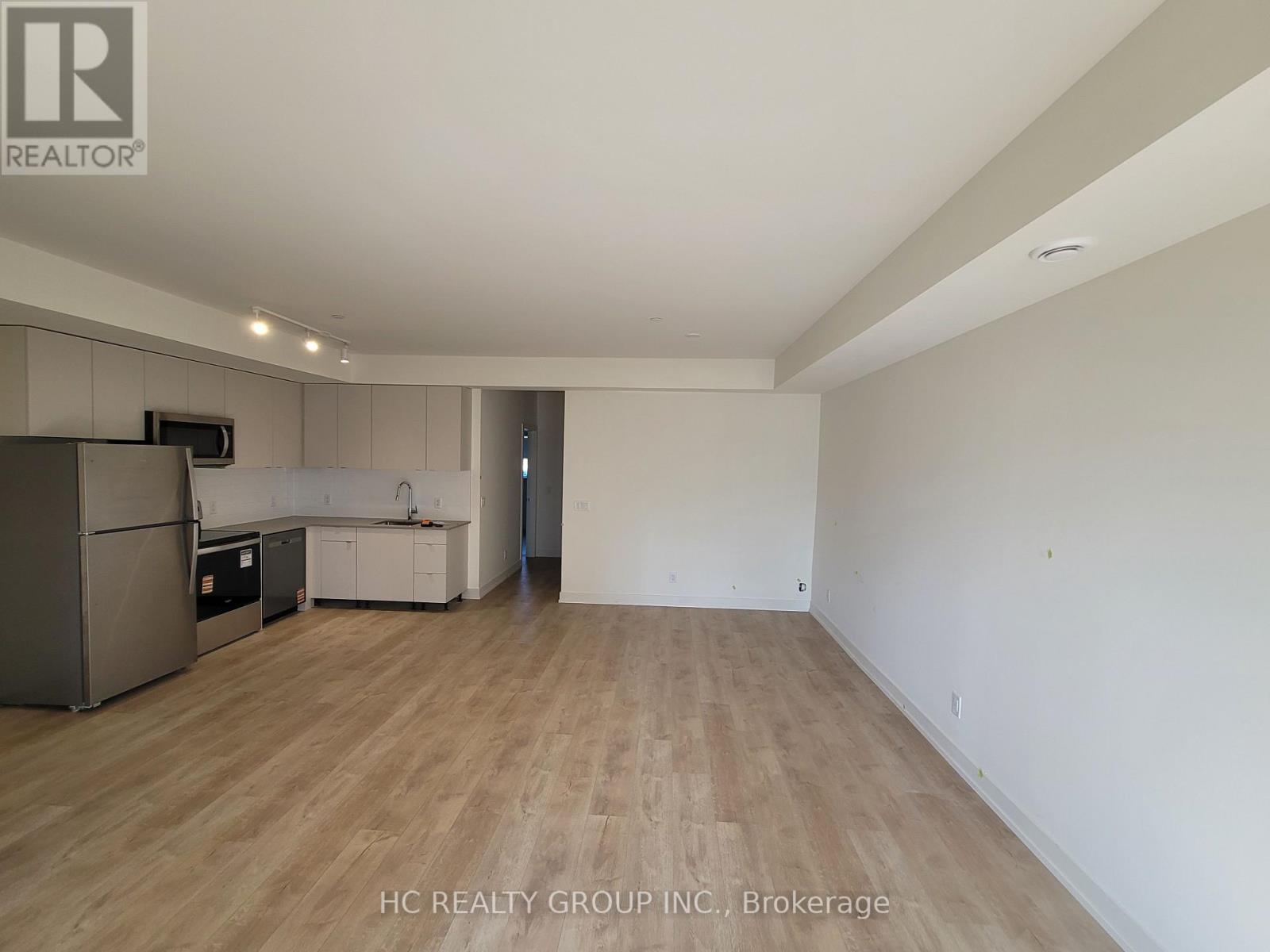 A spacious room with wooden flooring and a refrigerator in the corner.