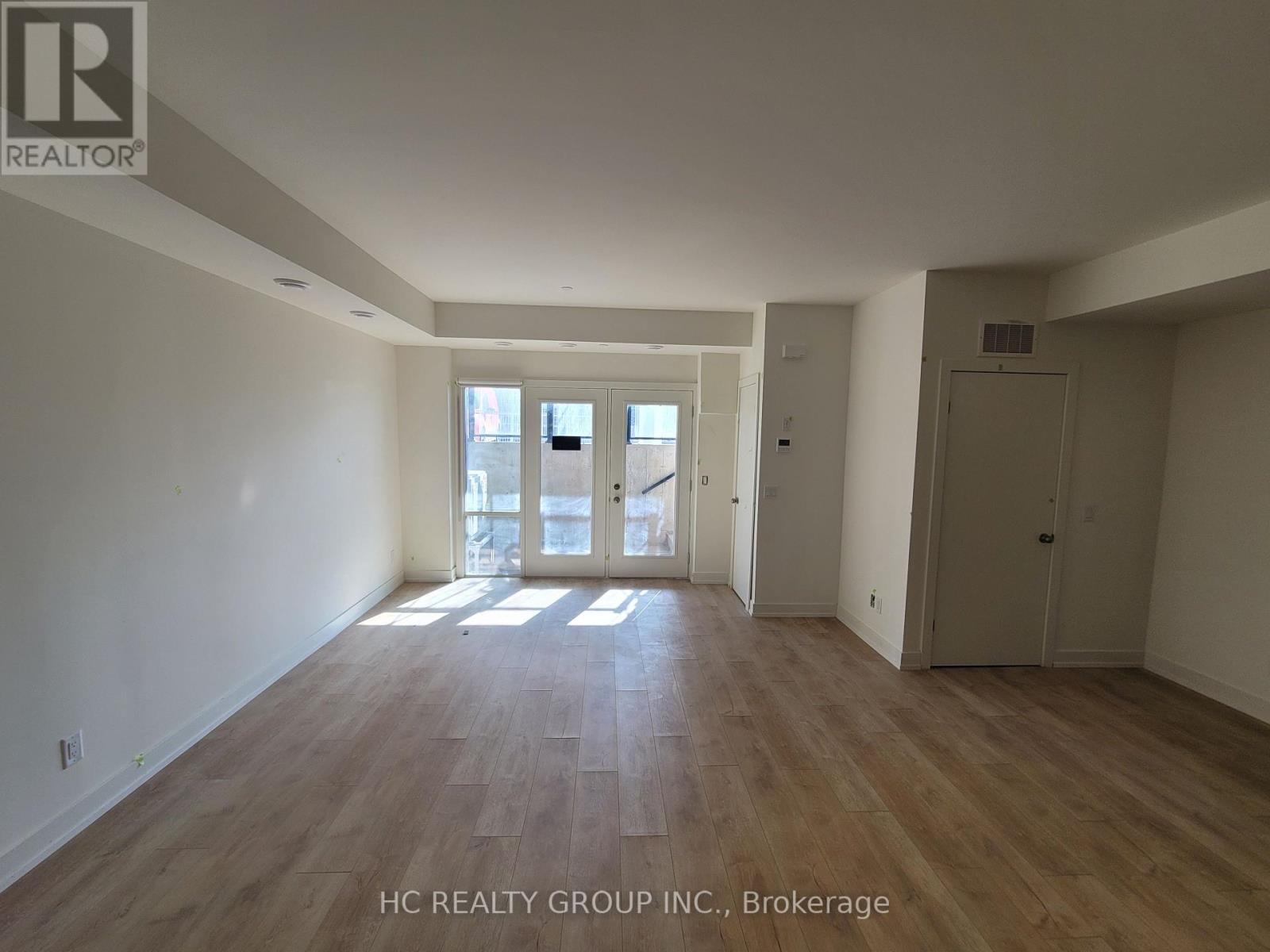 A spacious room with wooden flooring and white walls, with a door leading to a balcony.