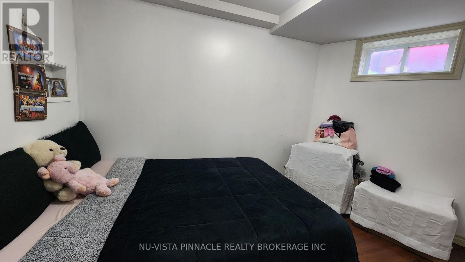 A bedroom with a bed, a teddy bear, and a person sitting on a bench.
