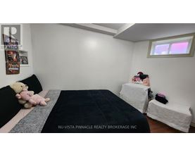 A bedroom with a bed, a teddy bear, and a person sitting on a bench.