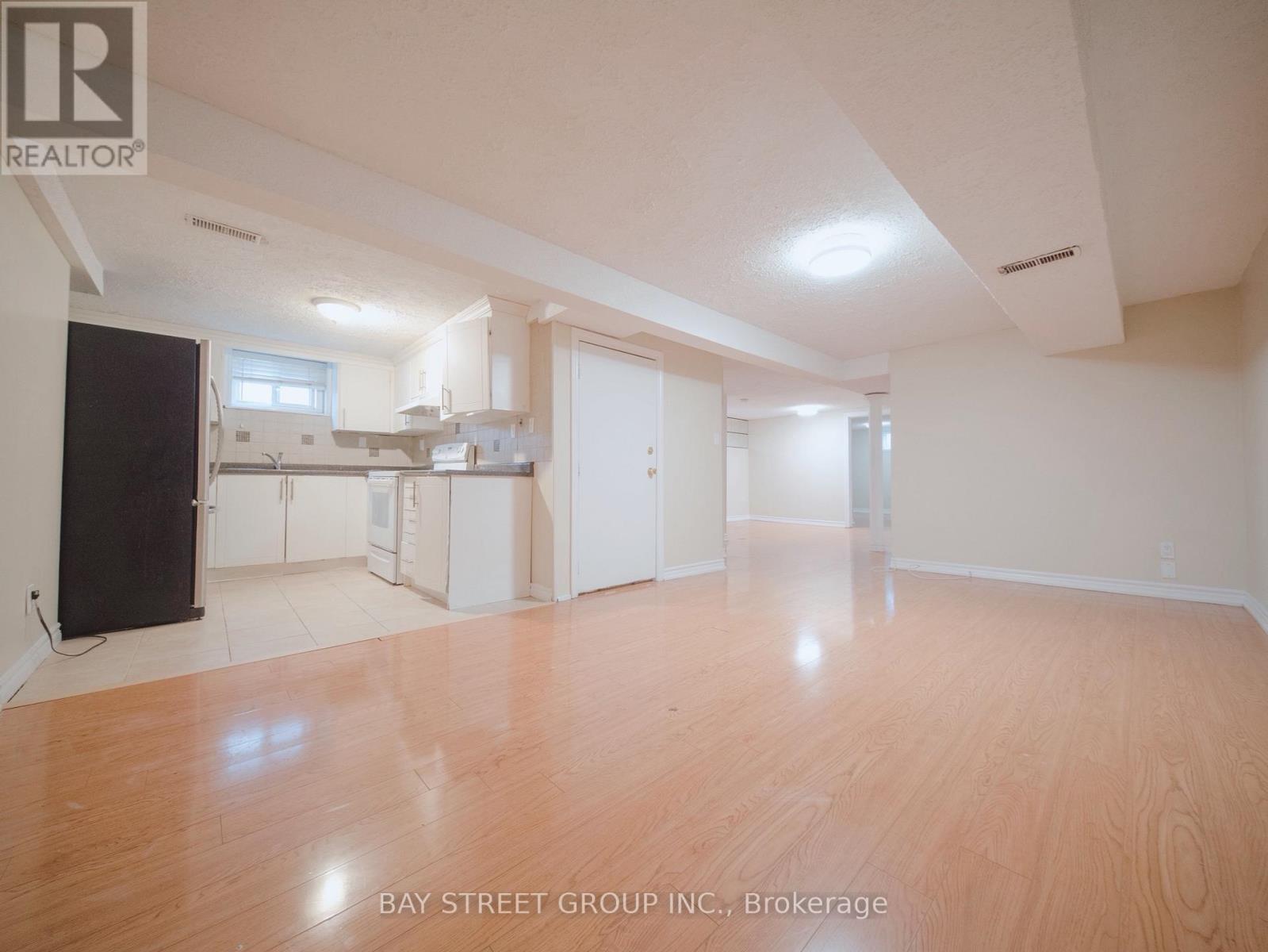 A spacious room with wooden flooring and white walls, with a kitchen area visible in the background.