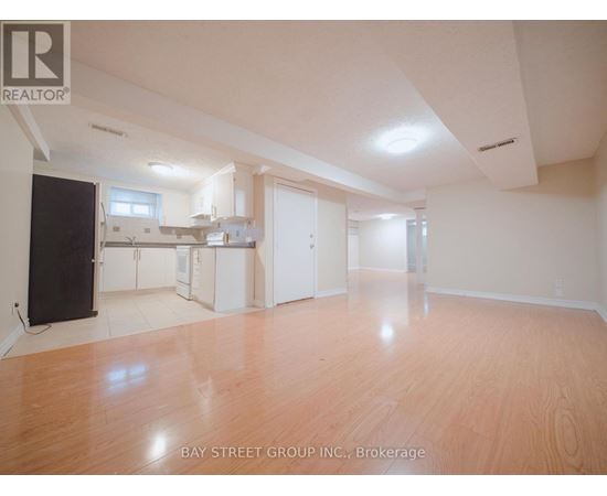 A spacious room with wooden flooring and white walls, with a kitchen area visible in the background.