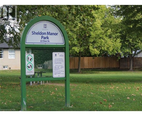 A green sign for Sheldon Manor Park is in front of a fence and trees.