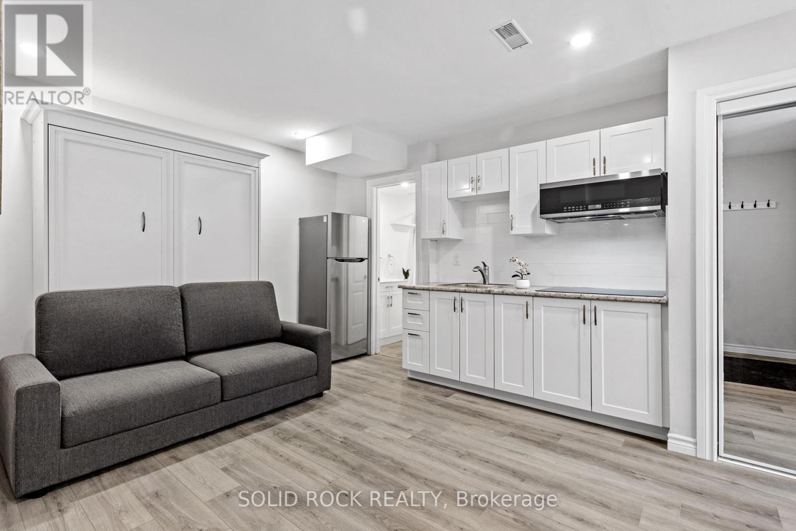 A grey couch sits in a white kitchen with wooden floors.