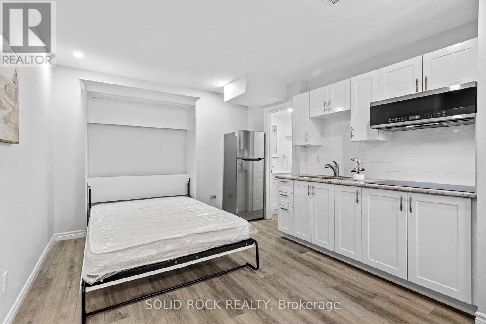 A bedroom with a bed, a refrigerator, and cabinets.
