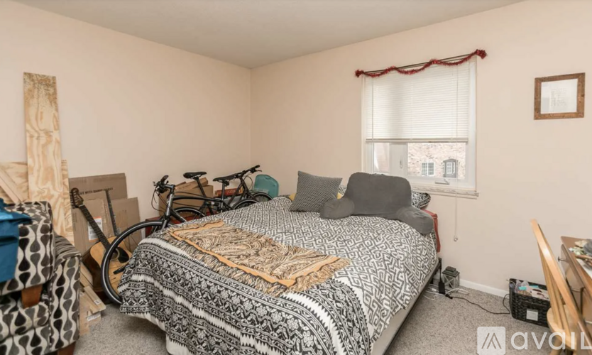 A room with a bed covered in a blanket and pillow, a bicycle, and a window with a view of buildings outside.
