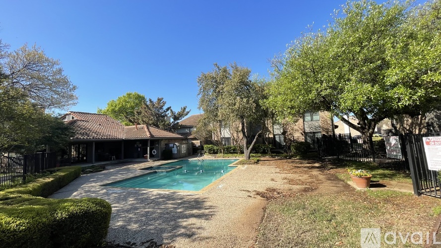 A pool surrounded by a fence and trees with a house in the background.