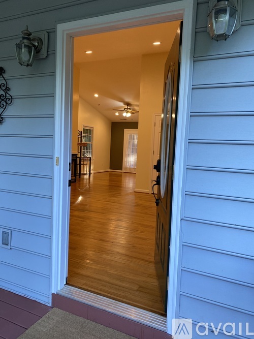 A white door opens to a hallway with wooden floors and a lamp on the wall.
