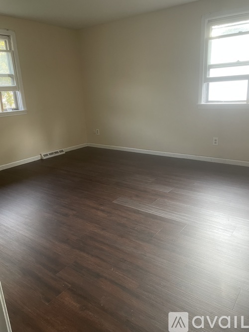 A room with wooden flooring and two windows.