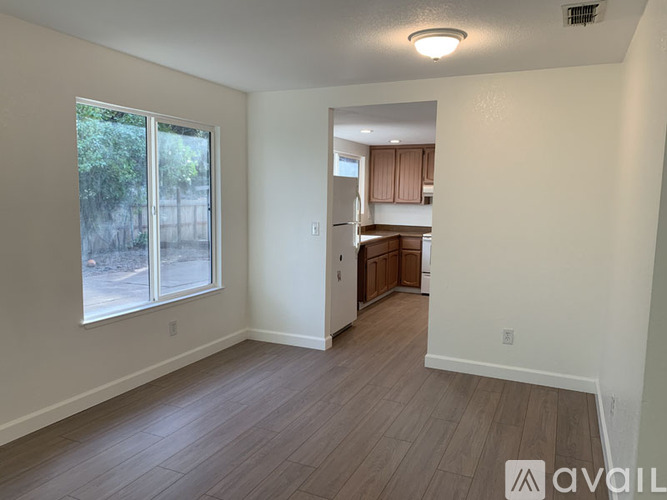 A room with a window and a kitchen area in the background.