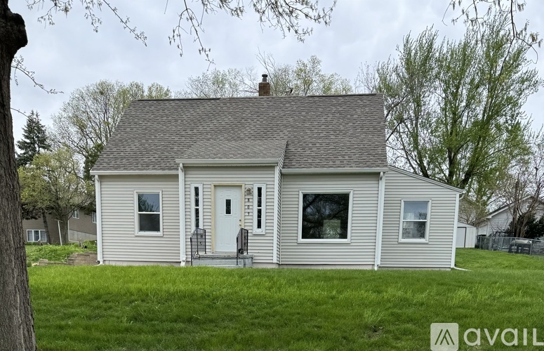 A small house with a white door and windows is surrounded by trees.
