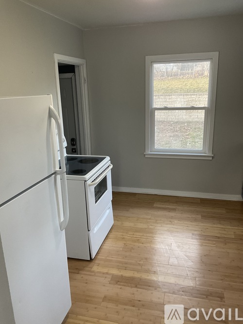 A white fridge and oven in a kitchen with wooden floors and a window.