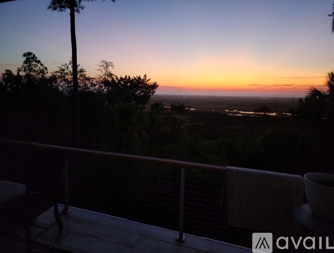A balcony overlooks a sunset with trees and a body of water.