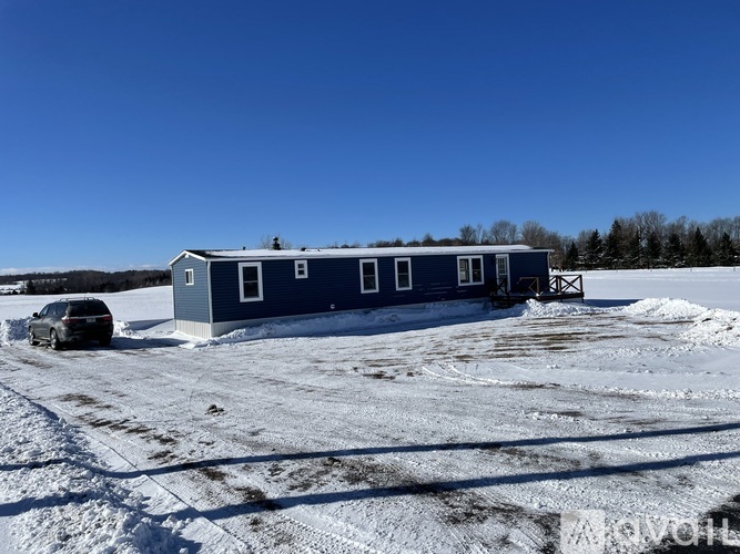 A blue house with a car parked in front of it on a snowy field.