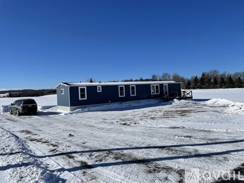 A blue house with a car parked in front of it on a snowy field.