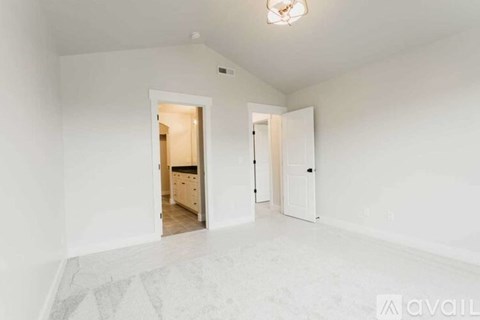 A spacious room with a white floor and walls, a ceiling light, and a doorway leading to another room.