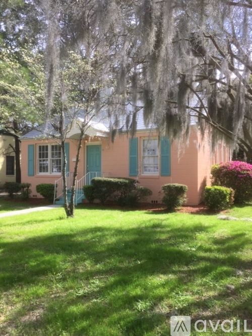 A house with a green lawn and trees with Spanish moss hanging from them.