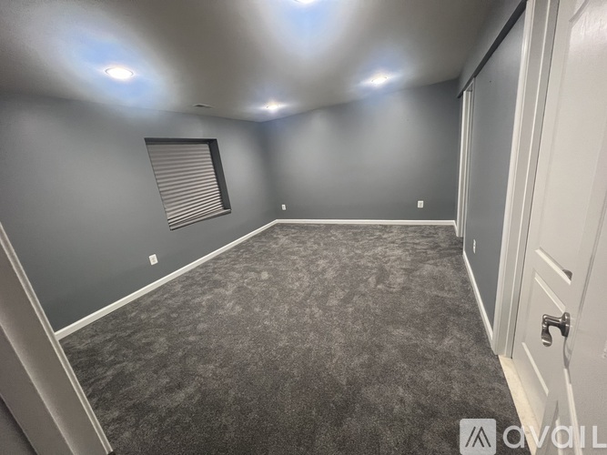 A room with grey walls and carpeting, a window with blinds, and a door.