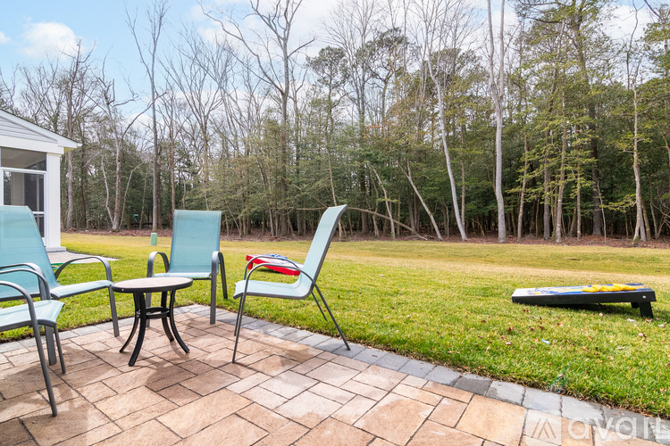 A patio with chairs and a table is surrounded by trees.
