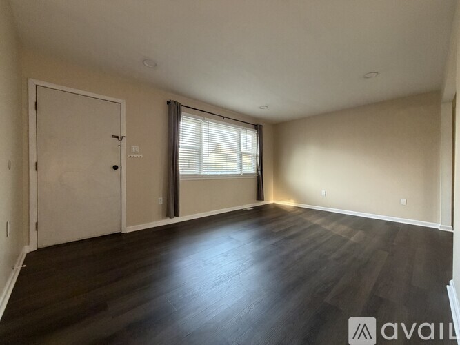 A spacious room with wooden floors and a large window with blinds.