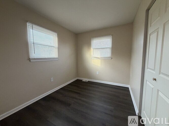 A room with a white door and two windows with blinds.