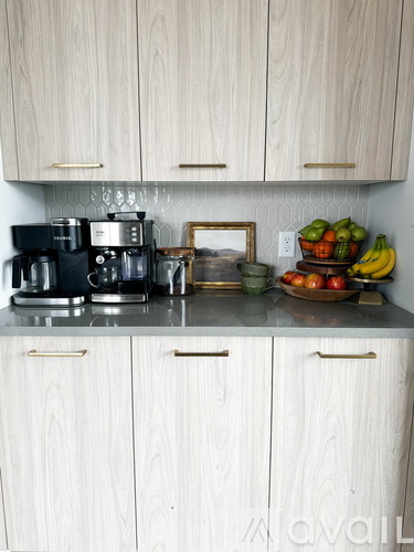 A kitchen with white cabinets and a countertop with a coffee maker, a picture frame, and a bowl of fruit.