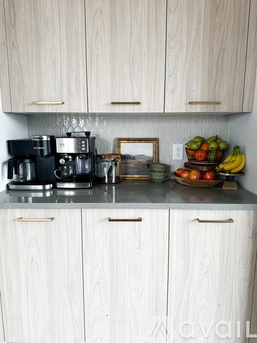 A kitchen with white cabinets and a countertop with a coffee maker, a picture frame, and a bowl of fruit.