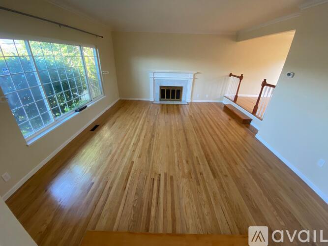 A spacious room with wooden flooring and a fireplace.