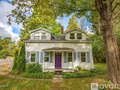 A white house with a purple door is surrounded by trees.