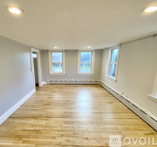 A spacious room with wooden flooring and two windows.