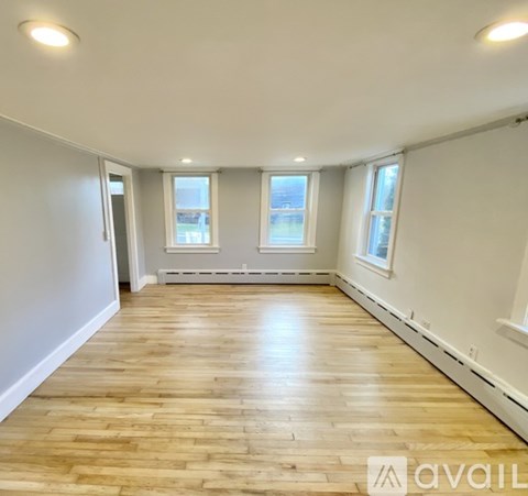 A spacious room with wooden flooring and two windows.
