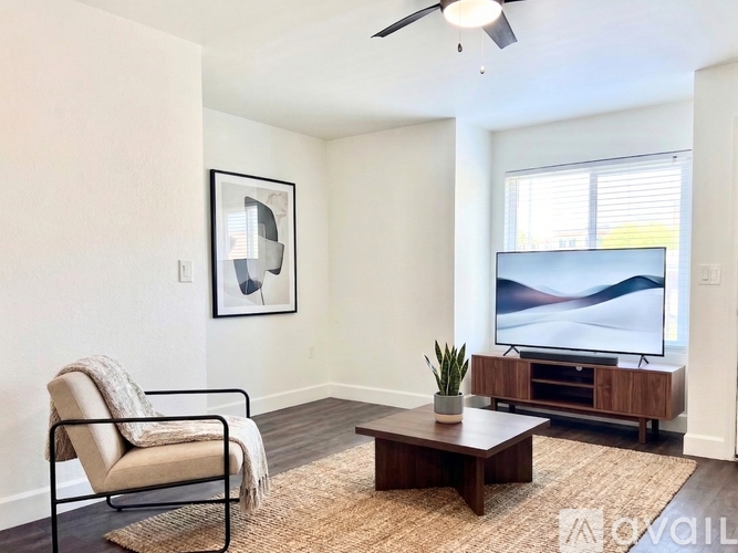 A living room with a chair, a table, a plant, and a television.