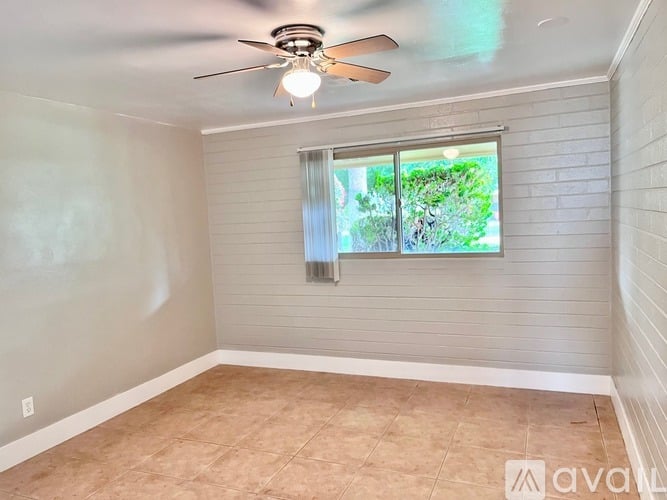 A room with a ceiling fan and a window with a view of trees.