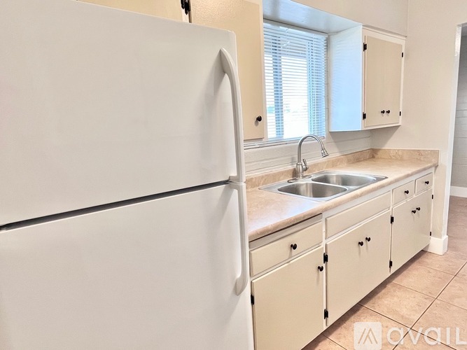 A white refrigerator is in a kitchen with a sink and cabinets.