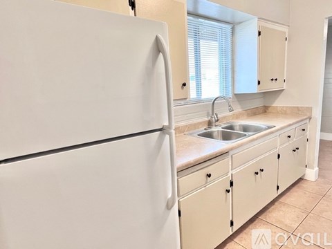 A white refrigerator is in a kitchen with a sink and cabinets.